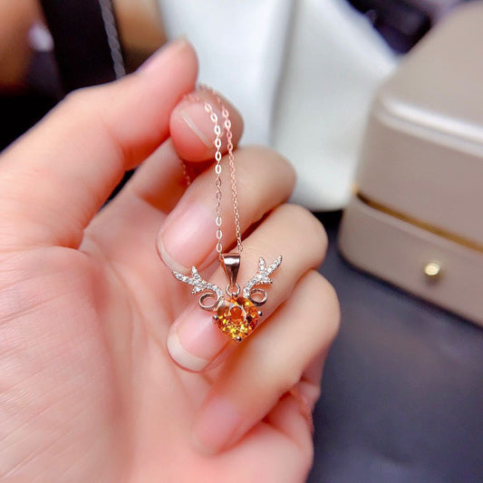 Hand holding a necklace with an orange gemstone pendant against a blurred background