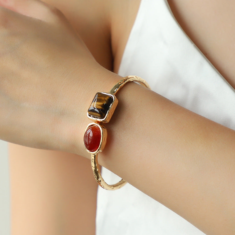 Gold bracelet with gemstones on a wrist against a neutral background