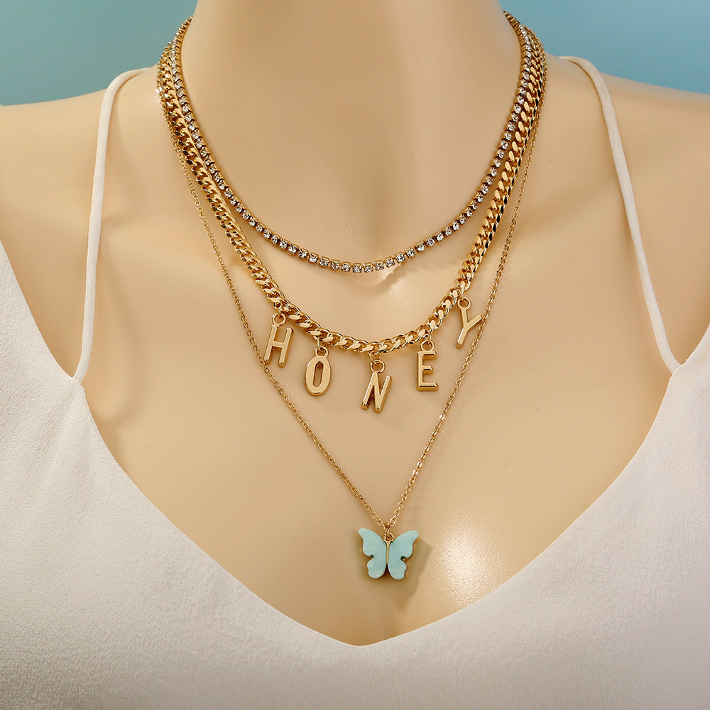 Gold necklaces with 'HONEY' and butterfly pendant on a mannequin with a light blue background