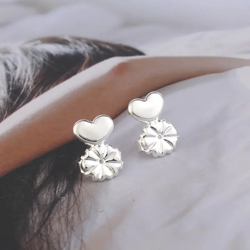 Silver heart-shaped earrings worn by a person with a neutral background