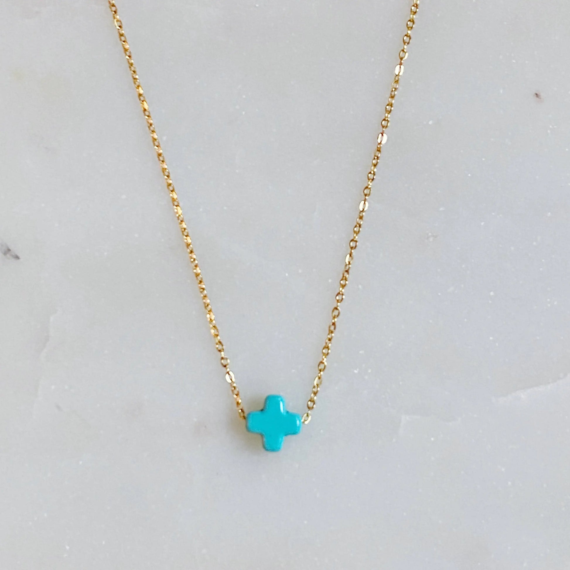 Gold necklace with a turquoise cross pendant on a light gray background