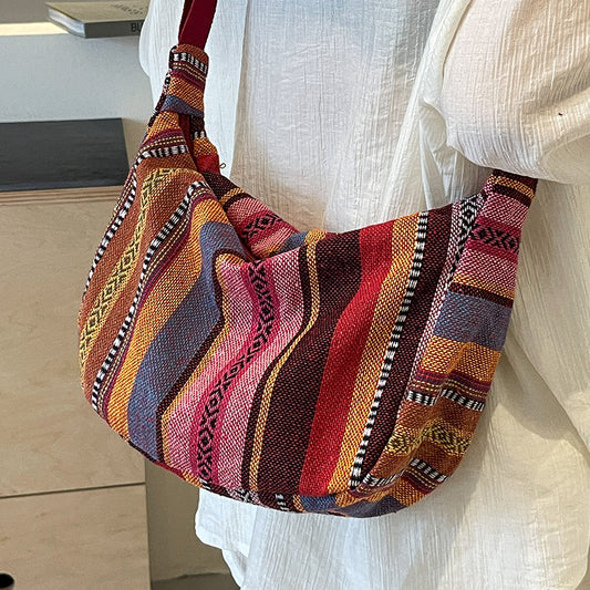 Multicolored patterned bag carried by a person wearing a white outfit.