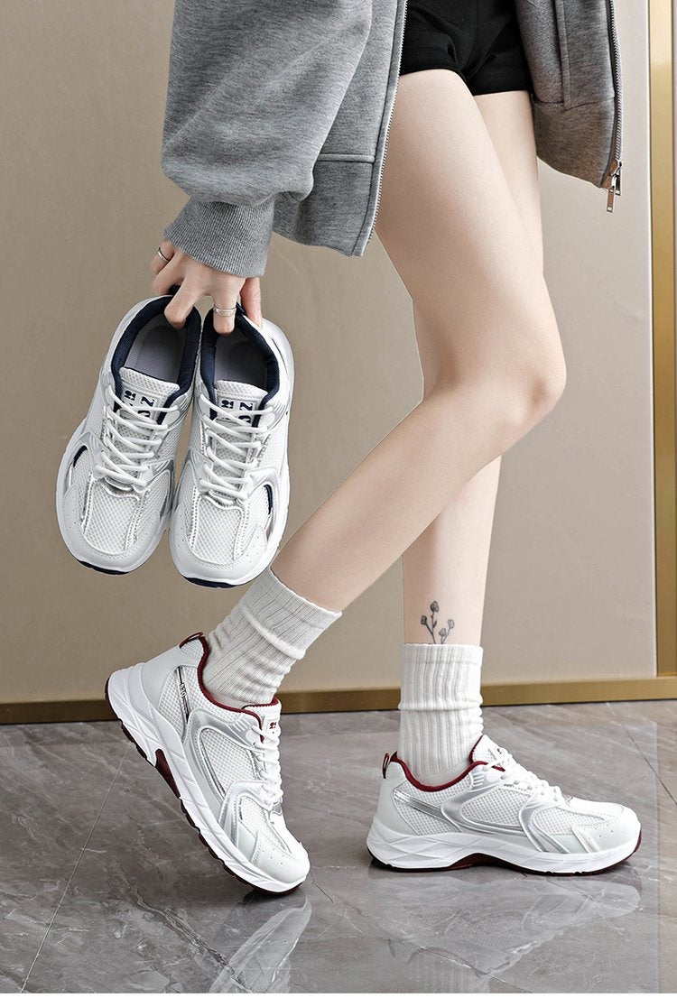Person wearing white sneakers and gray socks, holding a pair of white sneakers.