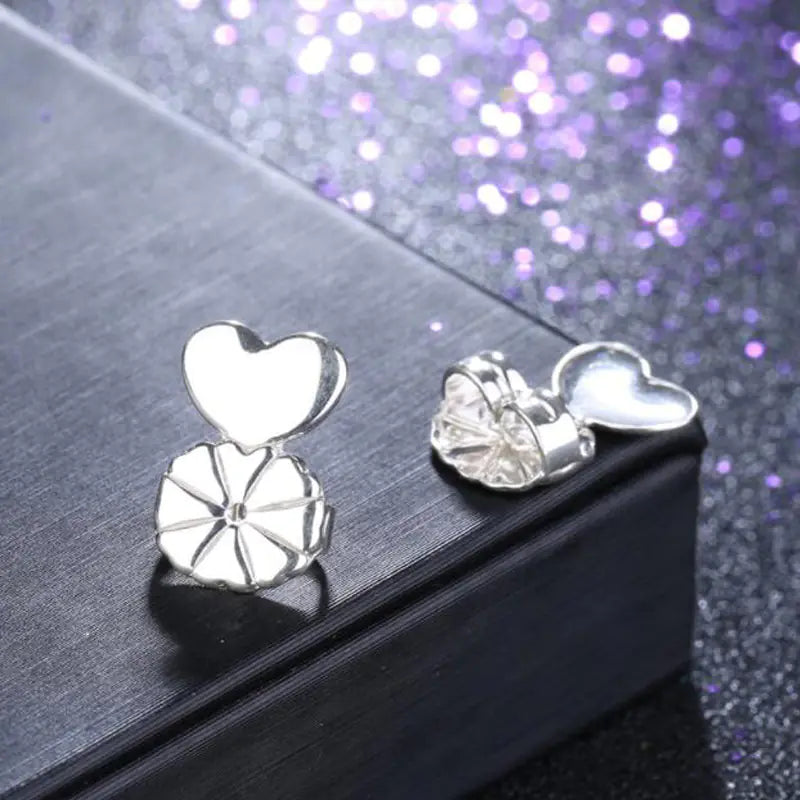 Silver heart-shaped earrings on a black surface with a glittery purple background