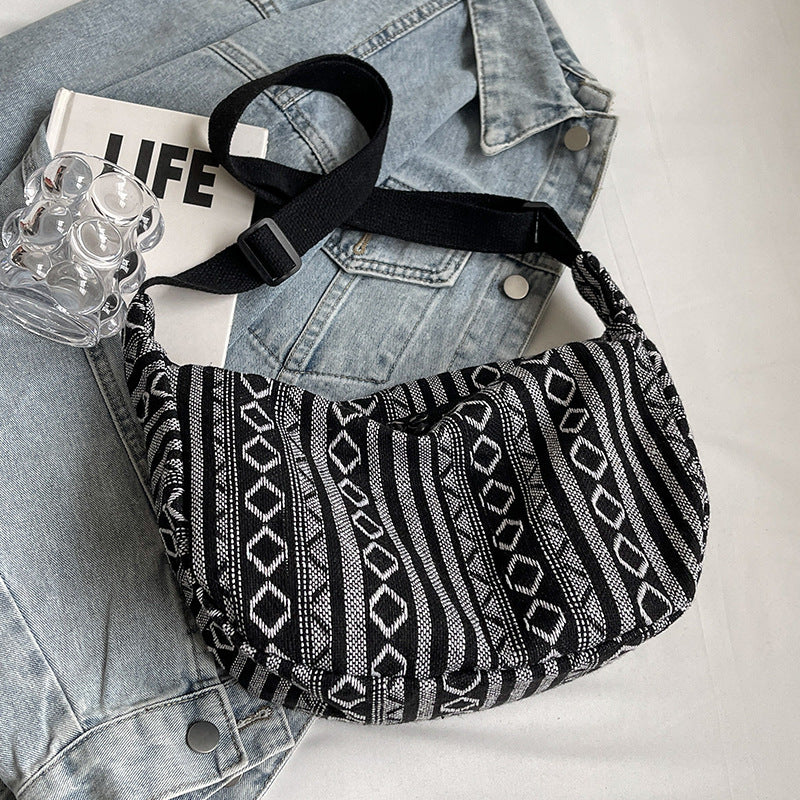 Black and white patterned bag on a denim jacket with a glass of water and a magazine.