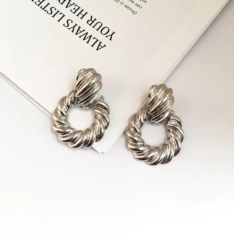Silver twisted hoop earrings on a white surface with text in the background