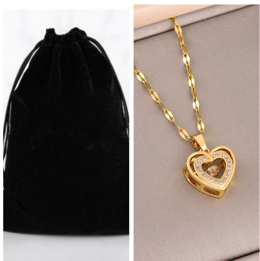 Gold heart-shaped necklace with chain on a gray surface next to a black velvet pouch.