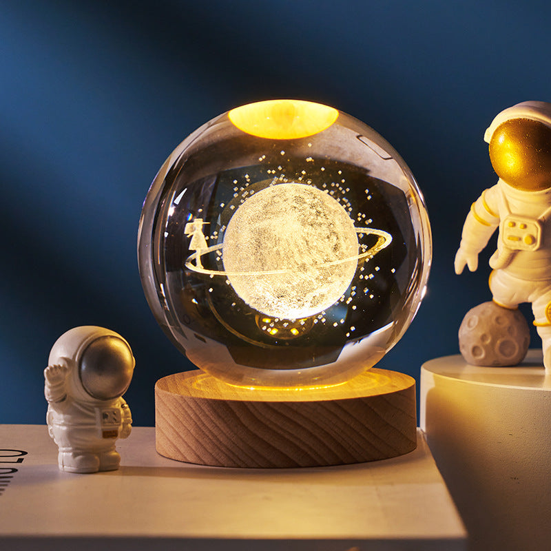 Glass orb with celestial design on a wooden base, surrounded by astronaut figurines against a dark blue background.