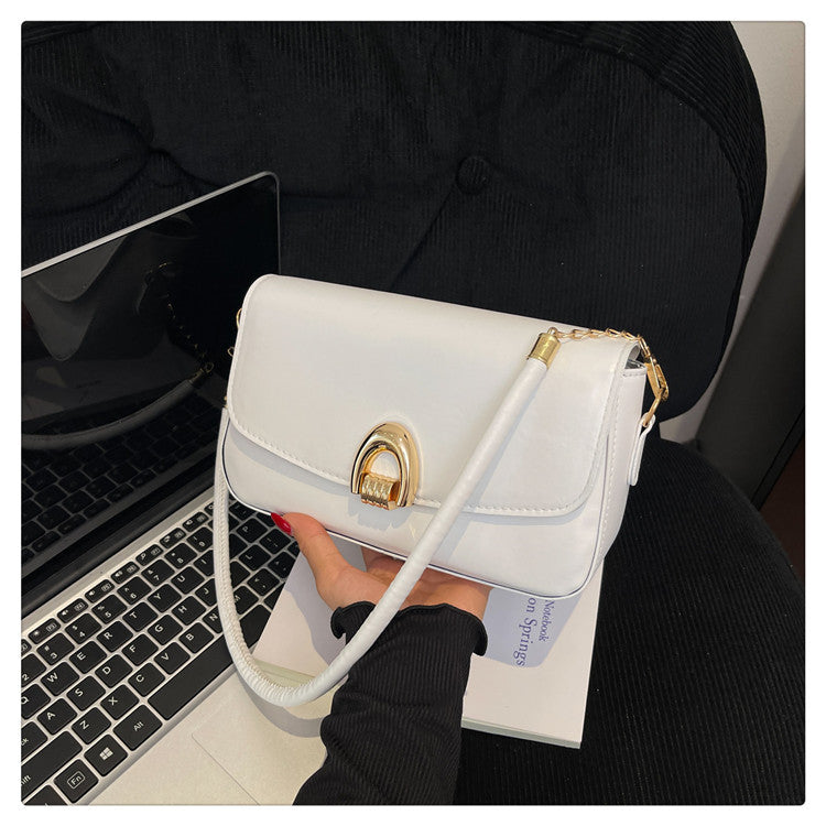 White handbag with gold accents held by a person in front of a laptop.