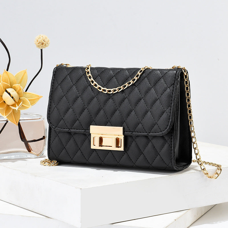 Black quilted handbag with gold chain strap on a white surface with decorative elements.