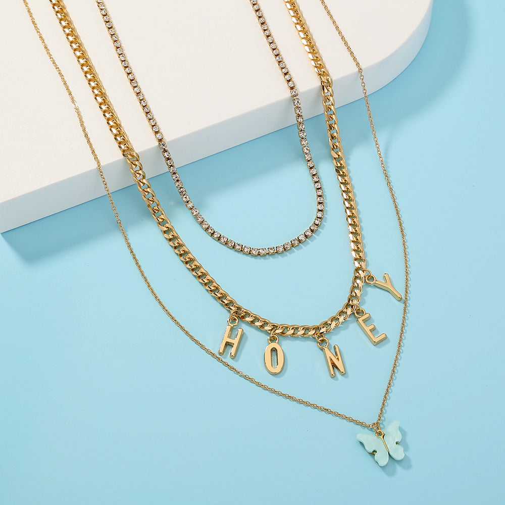 Gold necklaces with 'HONEY' and butterfly pendant on a light blue background