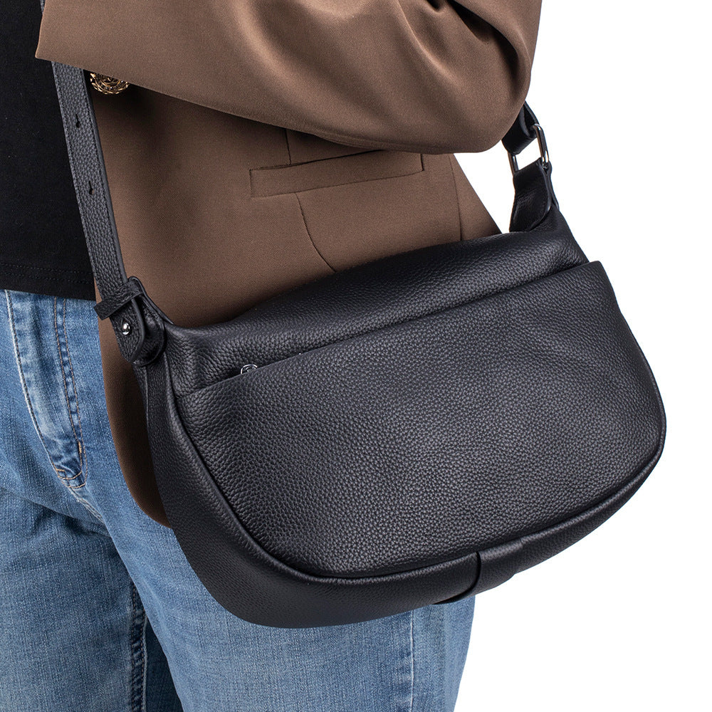 Person wearing a black leather shoulder bag with a neutral background
