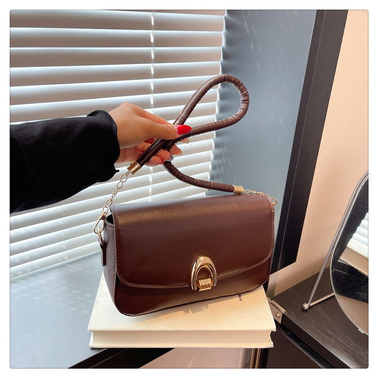 Brown handbag with a gold clasp held by a hand against a window background
