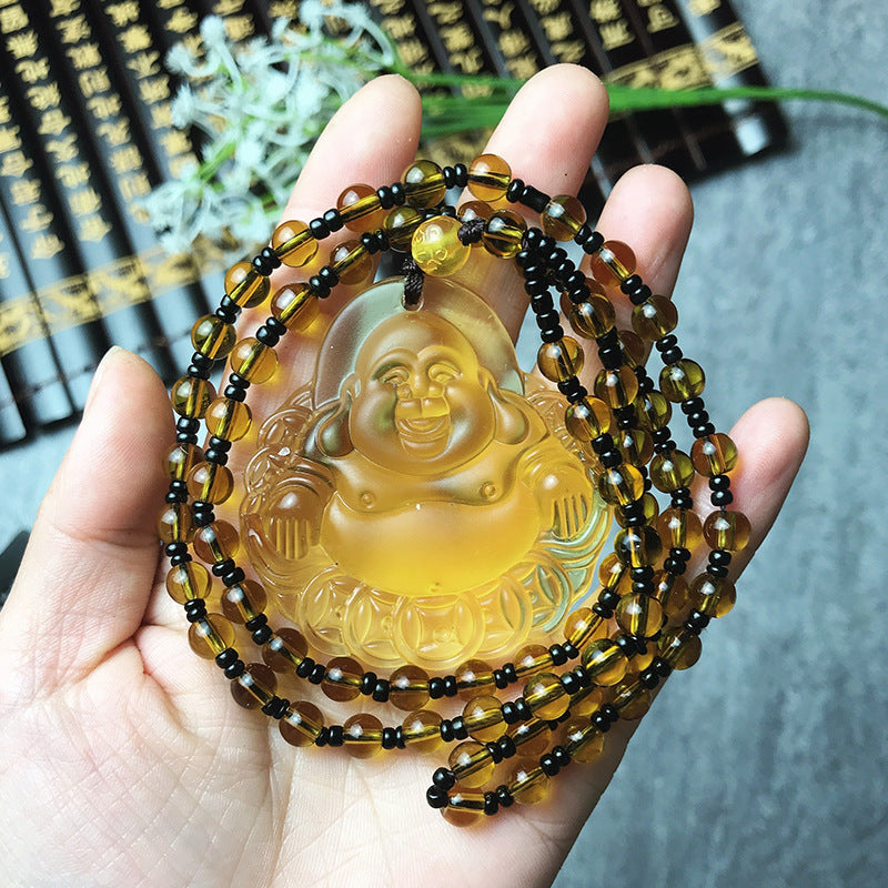 Hand holding a necklace with a Buddha pendant and beaded strands against a blurred background