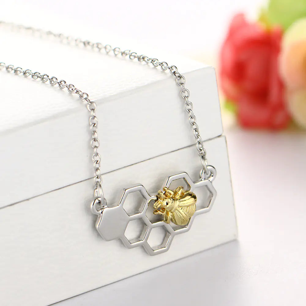 Necklace with gold bee and honeycomb design on a white surface with flowers in the background