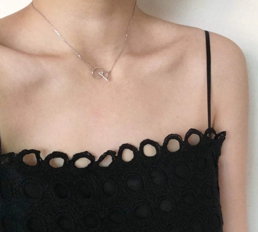 Person wearing a black lace top and silver necklace with a circular pendant.