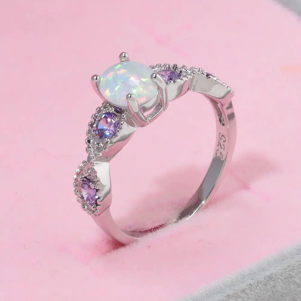 Silver ring with a white opal and purple gemstones on a pink background