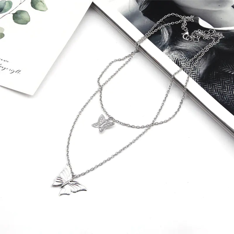 Silver butterfly necklace on a white surface with a magazine in the background
