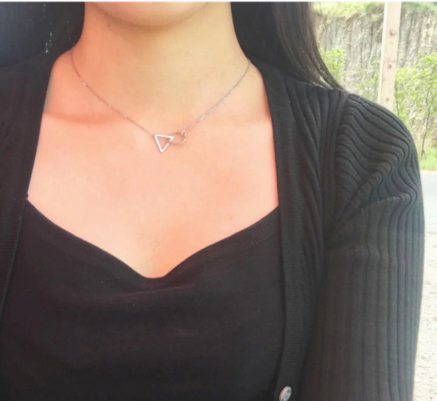 Person wearing a black top and a necklace with a triangle pendant.