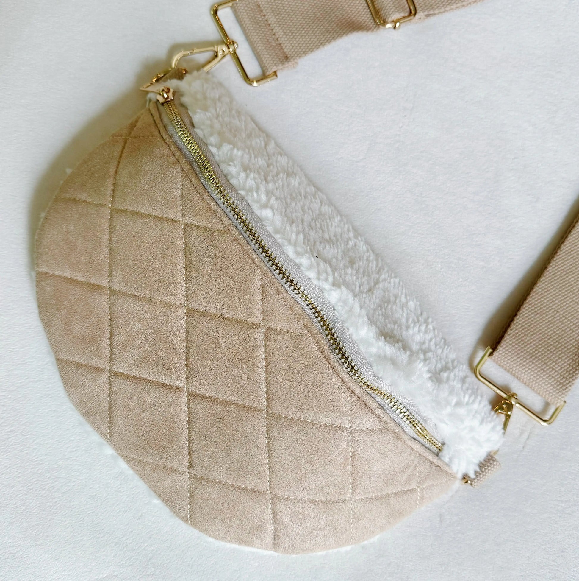 Beige quilted handbag with white interior and gold zipper on a light background