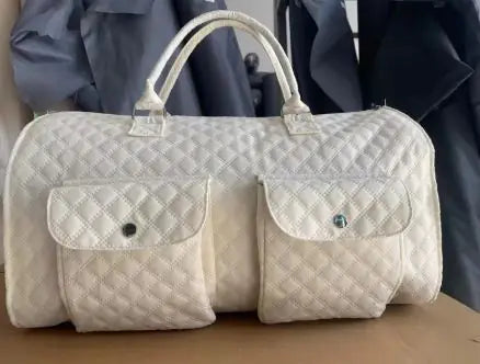 Quilted white duffel bag with two front pockets on a wooden surface.