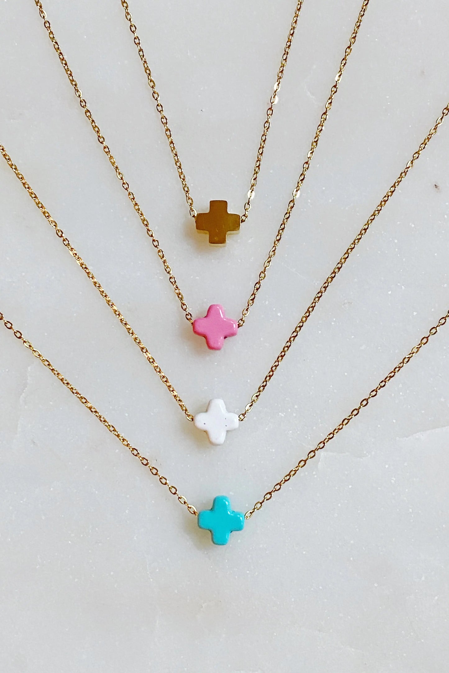 Three gold necklaces with colorful star pendants on a light gray background