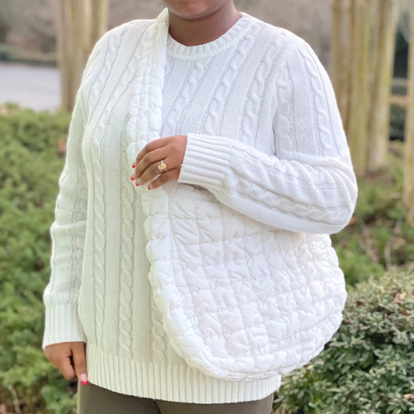 Person wearing a white cable knit sweater with a blurred background