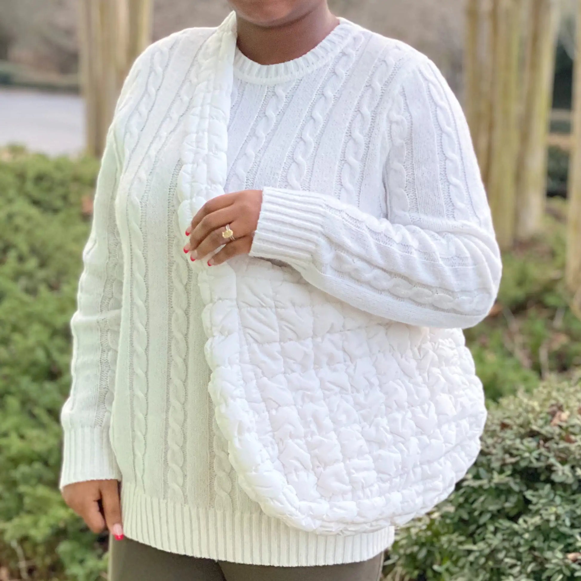 Person wearing a white cable knit sweater with a blurred background