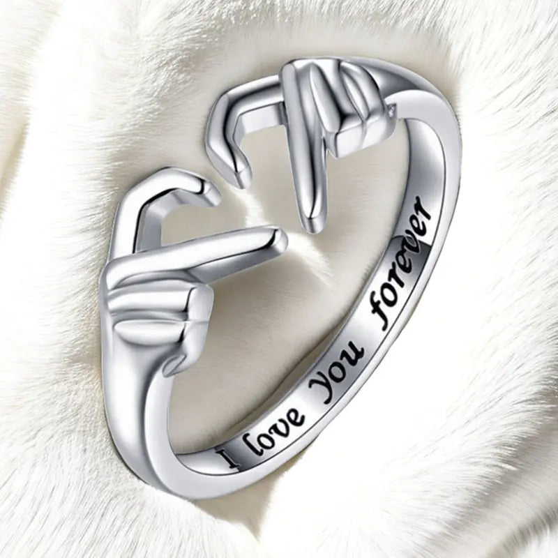 Silver ring with interlocking hands design and 'I love you forever' engraving on a white fur background