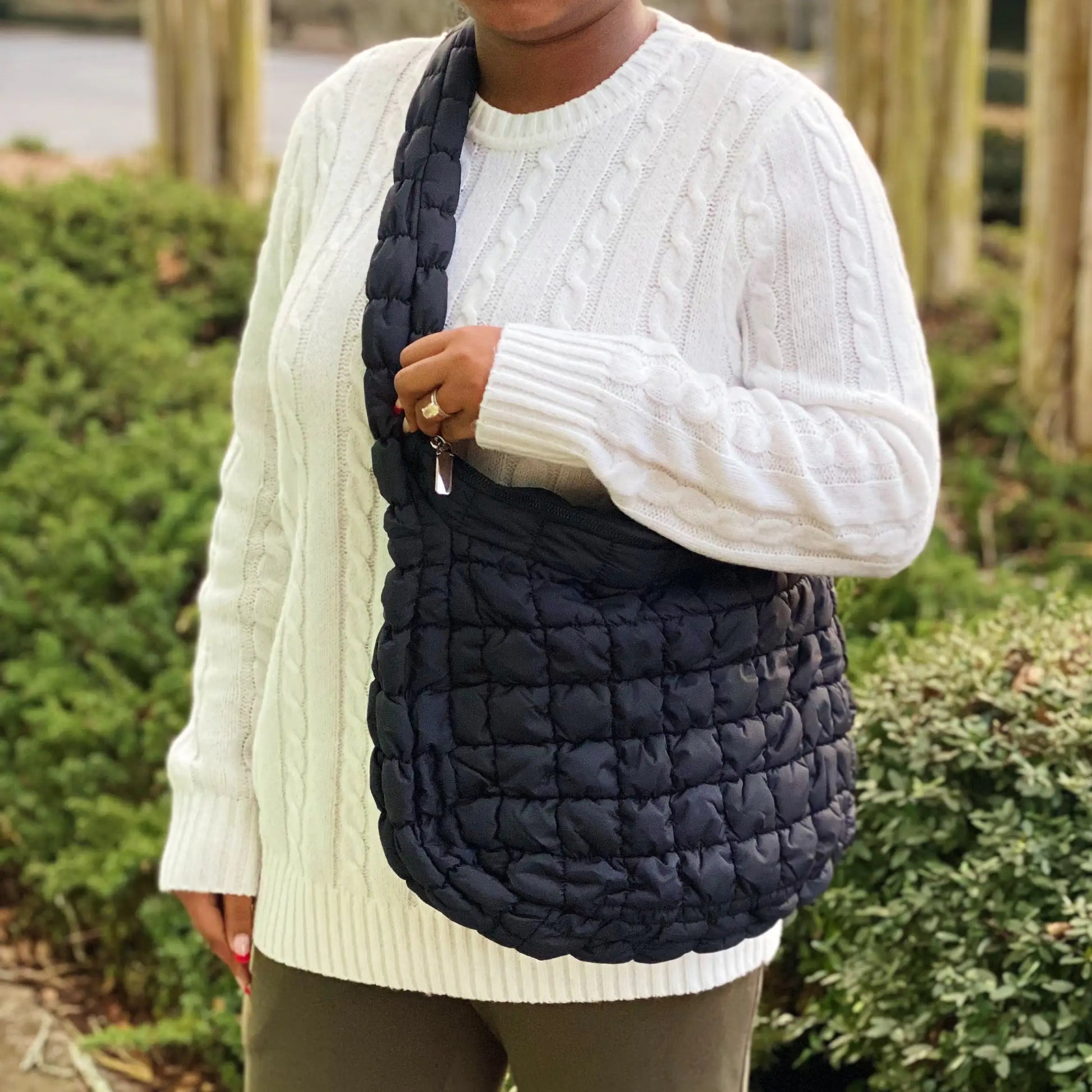 Person wearing a white sweater and holding a navy quilted bag outdoors.