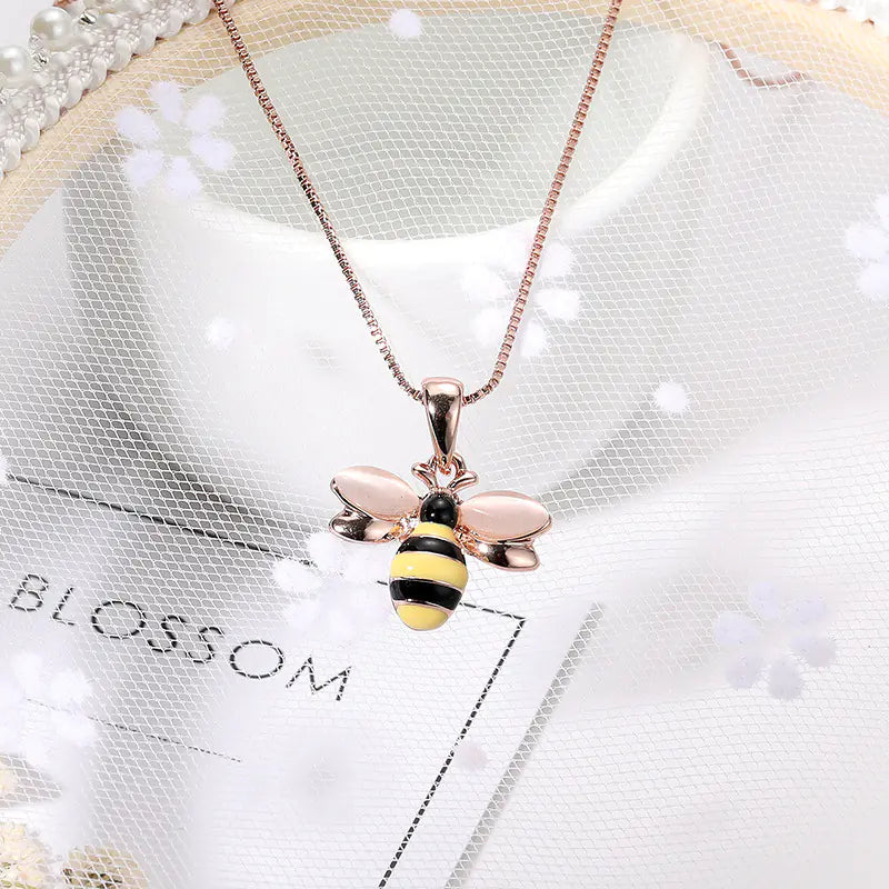 Rose gold bee pendant necklace on a white background with 'Blossom' branding.