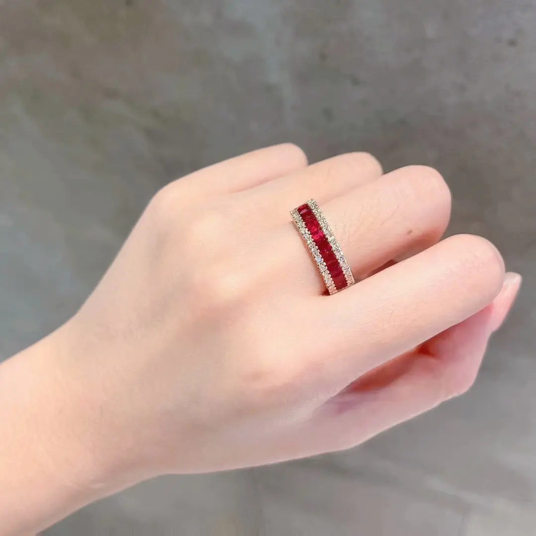 Hand wearing a ring with red gemstones on a neutral background