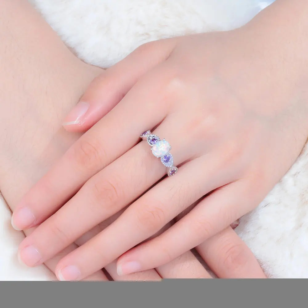 Close-up of a hand wearing a silver ring with purple and white stones on a white background