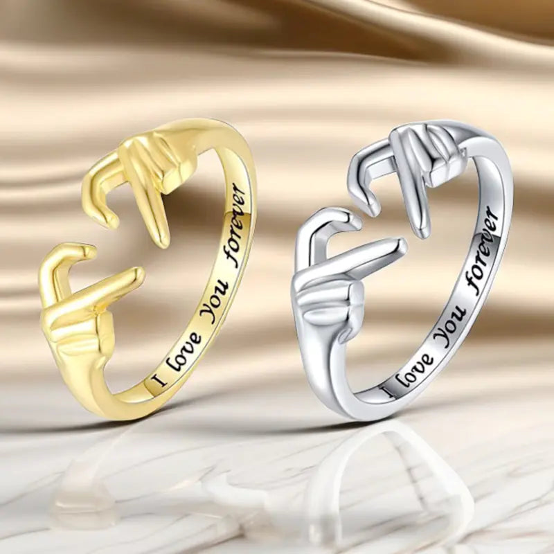 Gold and silver rings with 'I love you forever' engraving on a reflective surface.